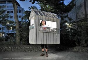 発泡スチロール製の白い家の中に身を置く村上さん。約1年間、この家を背負いながら国内180か所を移動してまわった。（撮影：Ken'ichiKikuchi）