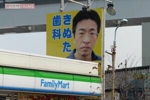 『きぬた歯科』看板マニアが260箇所から選ぶ「オススメ看板3選」その2 「川崎街道と多摩都市モノレールが交わる箇所、ファミリーマート日野高幡店前にあります。当初は笑顔の院長の写真でしたが、ファミリーマートに阻まれた関係でデザイン変更を余儀なくされることに。結局怪訝な表情の院長が張り重ねられ、今に至ります」（『看板研究家』D.J.マメ氏）