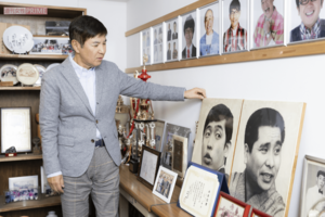 事務所の大先輩である萩本欽一、故・坂上二郎さんのパネルの前で。「要所要所で萩本さんからいただいたアドバイスのおかげでここまでくることができました」　撮影／矢島泰輔