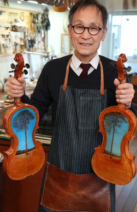 津波ヴァイオリンとヴィオラを持つ中澤氏。裏には“奇跡の一本松”の絵が描かれている