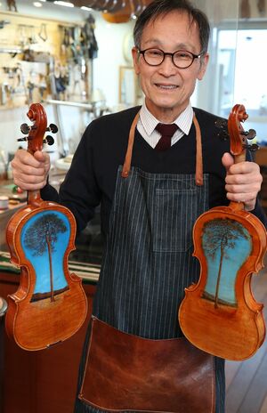 津波ヴァイオリンとヴィオラを持つ中澤氏。裏には“奇跡の一本松”の絵が描かれている