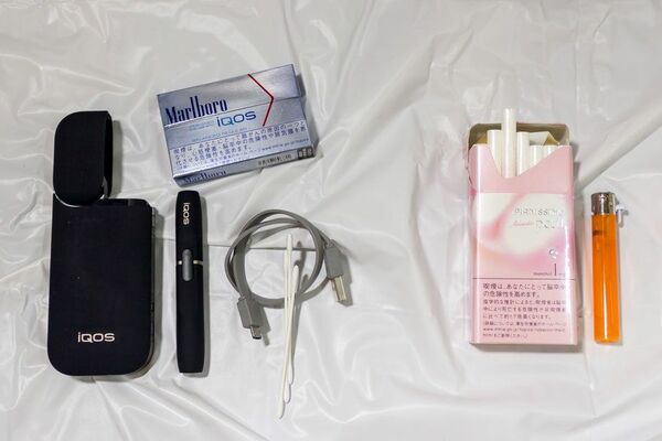 右側が従来の紙巻きタバコとライター。左側が専用ヒートスティック、アイコス本体、ポケットチャージャー、充電用のケーブル、綿棒