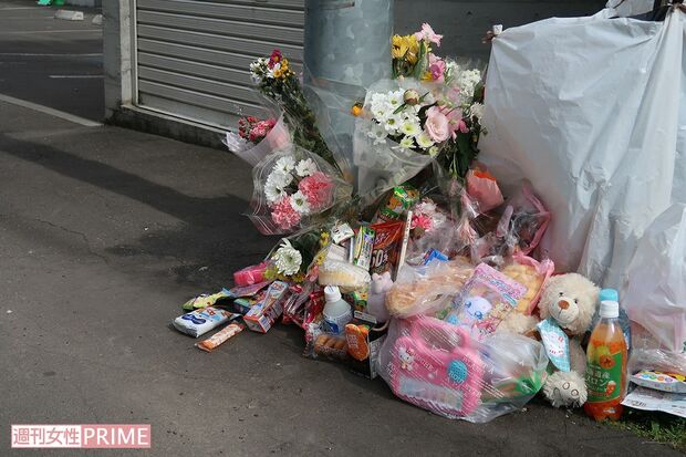 現場マンション前には献花でいっぱいに……