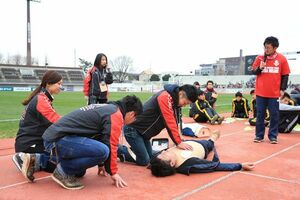 ［写真］試合前のピッチ脇で行われたAED講習会。済生会前橋病院の医師・看護師らが、救命法のデモンストレーションや、高校生たちに直接、心臓マッサージやAEDの指導を行った