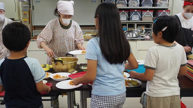 ボランティアがよそう料理を子どもたちが自分で取りにいく