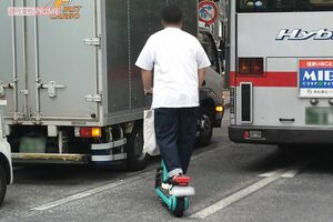 電動キックボードでバス横をすり抜ける若い男性