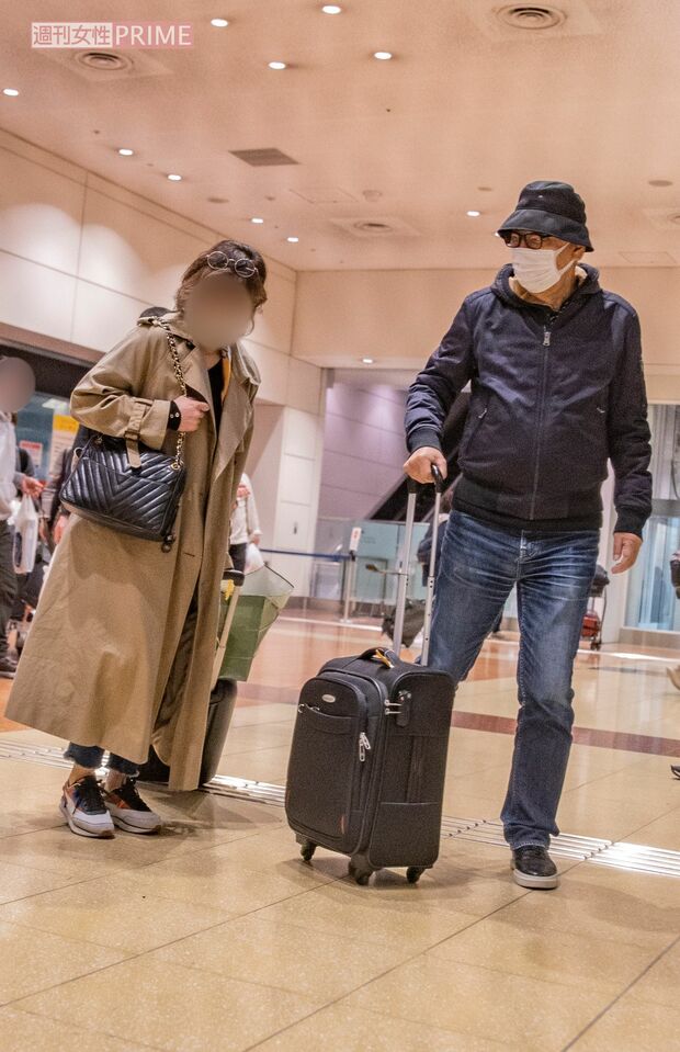 3月中旬、数泊分の荷物とともに羽田空港の到着口から出てきた岸部一徳と女性。バスを待つ間もイスに並んで座って話し続けた