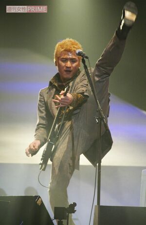 ギターを弾きながら足を高く上げる吉川晃司(2004年、20周年記念ライブにて)