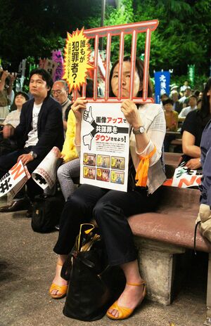 市民の集いで「NO!」の声を上げる参加者。“鉄格子”越しにスピーチを聞く女性も