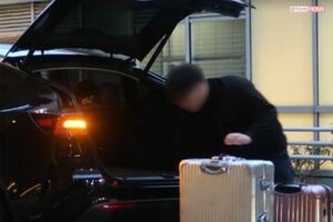 ハイヤーに黄皓と女性のスーツケースを積む運転手、シルバーのスーツケースの横にピンクのスーツケースが