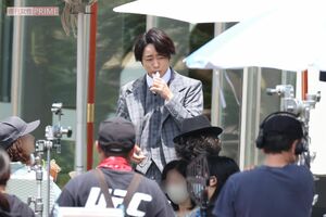 ゼリー飲料を口に運ぶ櫻井翔。炎天下の撮影に抜かりはない