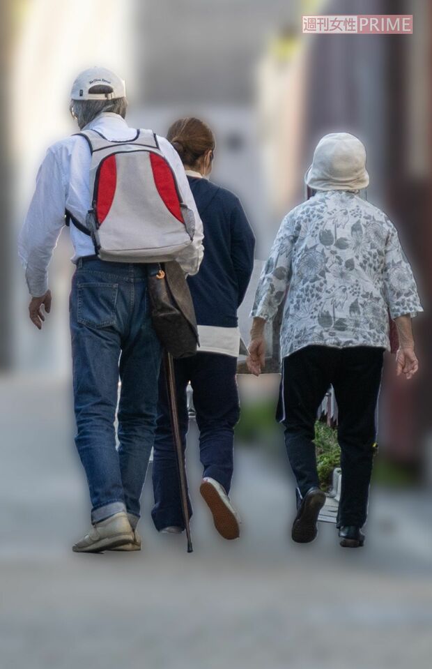 ヘルパーに付き添われた妻のひかるさん（右）に寄り添い、杖をつきながら散歩に向かった山崎（左）