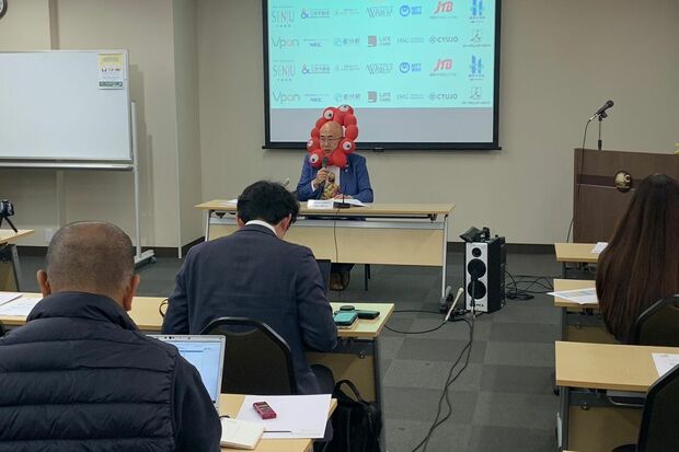 ミャクミャクのぬいぐるみをつけたまま会見をする大阪観光局理事長・溝畑宏さん