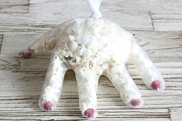 【ポップコーンハンド】ポリエチレンの手袋を用意。指先の部分にマーブルチョコ（赤）を1個ずつ詰める。ポップコーンを手首の手前ぐらいまで詰めたら、手首部分を結んで留める。　『可愛くって ホラーで 美味しい！ キモめし』より