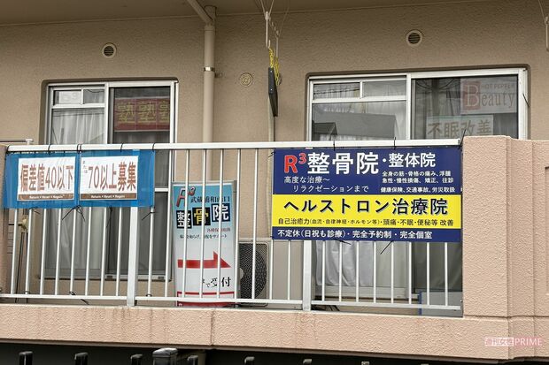 反対側の窓やベランダの手すりなどそこかしこに『アール・キューブド武蔵浦和西口整骨院』宣伝の貼り紙が（画像は一部加工しています）