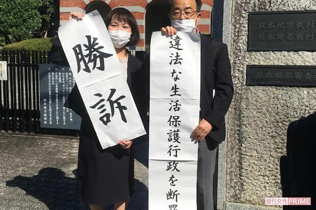 生活保護廃止処分の取り消しを求める裁判後、熊本地裁前で勝訴の旗を掲げる原告側弁護士ら