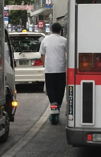 電動キックボードでバス横をすり抜ける若い男性