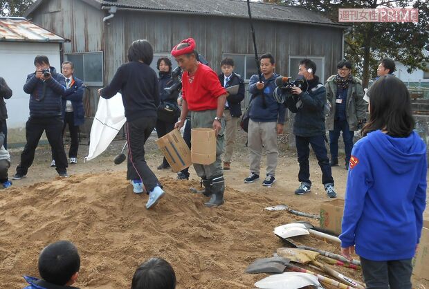 赤いハチマキを巻いて土のうの作り方を教える＝12月10日、日出町立川崎小で