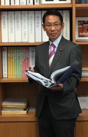 議員バッジをつけて書棚の前に立つ椎木保容疑者（本人のブログより）