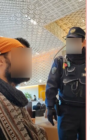 拡散している、ホテルに居座る外国人男性の荷物を確認しようとするに警察官が退去を求める動画の一部。外国人は目をつぶっている