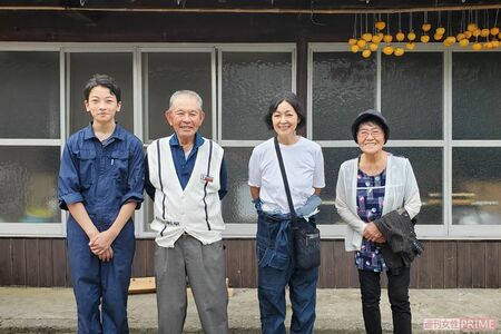 後ろにつるされた大量の干し柿はこの時季の風物詩。畑に隣接するこの古い家を建て替えた