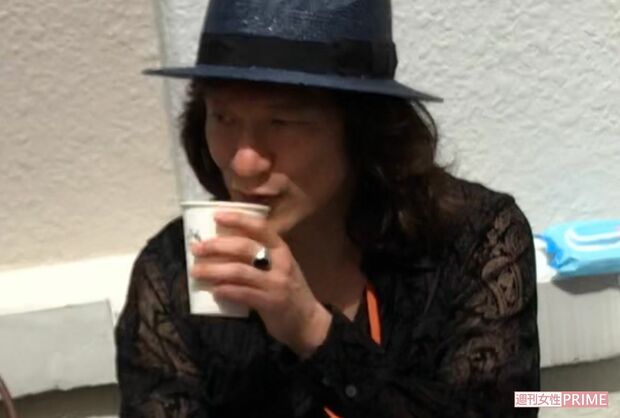 座ってカップを手にするユカイ（'18年5月）