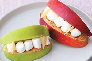 【ドラキュラの入れ歯】りんごにピーナツバターを塗り、ミニマシュマロをサンドしたら完成。りんごは厚さ1．5cmぐらいに切るとバランスがいい。牙の形に切ったアーモンドをさして雰囲気アップ。　『可愛くって ホラーで 美味しい！ キモめし』より