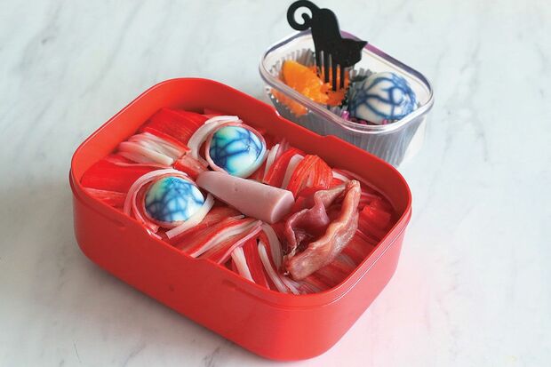 【顔面筋肉のお弁当】細かく裂いたかに風味かまぼこで筋肉っぽさを表現したお弁当。お弁当箱にごはんを詰め、目、鼻、口部分をへこませ、かに風味かまぼこを筋肉のようにのせる。目にうずら卵、鼻に魚肉ソーセージ、唇に生ハムを使用した。　『可愛くって ホラーで 美味しい！ キモめし』より