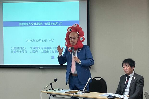 ミャクミャクのぬいぐるみをつけたまま会見をする大阪観光局理事長・溝畑宏さん