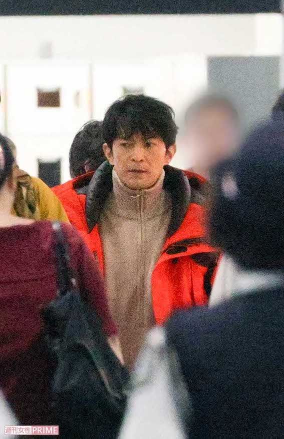 赤いダウンジャケットの中にフリースのインナーを着て、人混みの中を歩く津田健次郎は、続編からの新キャスト