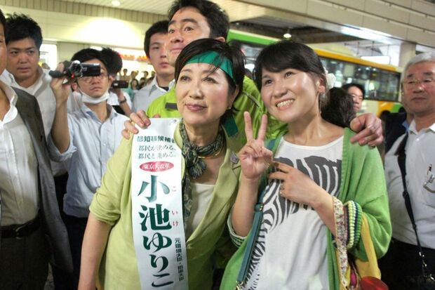 小池カラーをまとった女性と記念撮影。後ろはアルピニスト野口健氏＝JR王子駅前