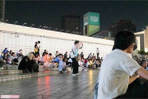 端に寄って、手元の媒体でライブを見届けるファンたち