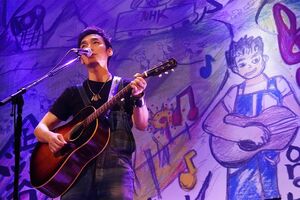 自画像とのツーショットでギターを弾くつよぽん。ほんのり似てる……？